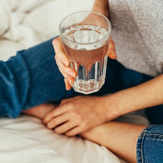 Persona sentada en la cama sosteniendo un vaso de agua filtrada